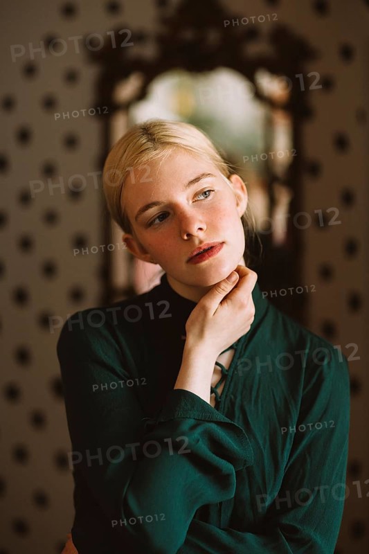 A serene portrait of a teenager in a green shirt, thoughtfully posing indoors against a stylish patterned background, capturing a moment of introspection