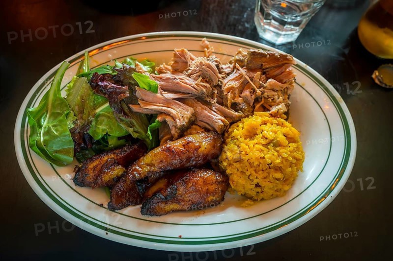 Vibrant plate showcasing a delicious and satisfying caribbean inspired meal, featuring tender pulled pork, sweet fried plantains, seasoned yellow rice, and a crisp green salad