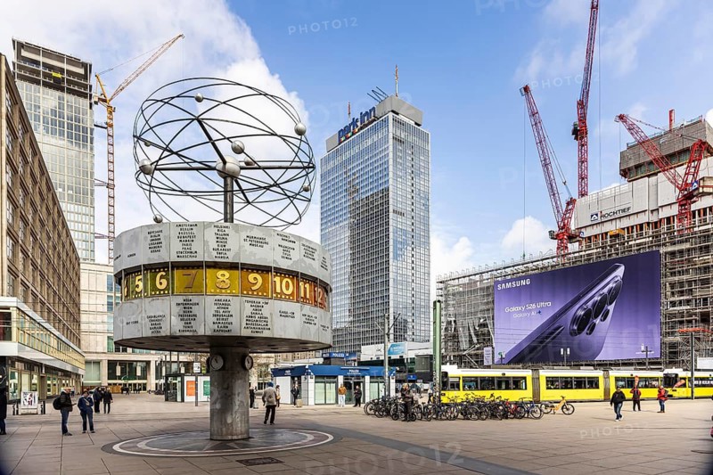 View of Alexanderplatz in Berlin. Covivio Tower construction site. Landmark world clock. Behind it, a mega poster and a tram. Berlin, Germany