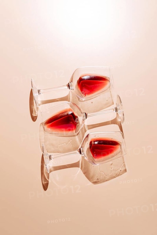 Three glasses of red wine placed on a flat surface, casting intriguing reflections. The light and shadow play creates an artistic composition, perfect for wine-related content