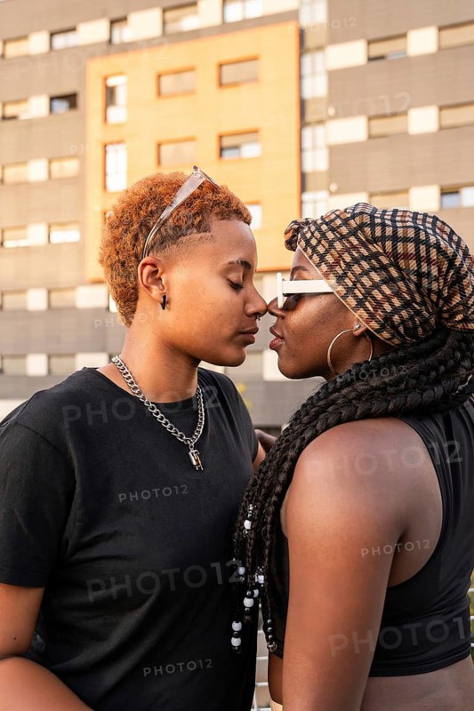 A loving LGBT multiethnic couple shares an intimate moment on a city rooftop, close and affectionate, with vibrant urban architecture in the background