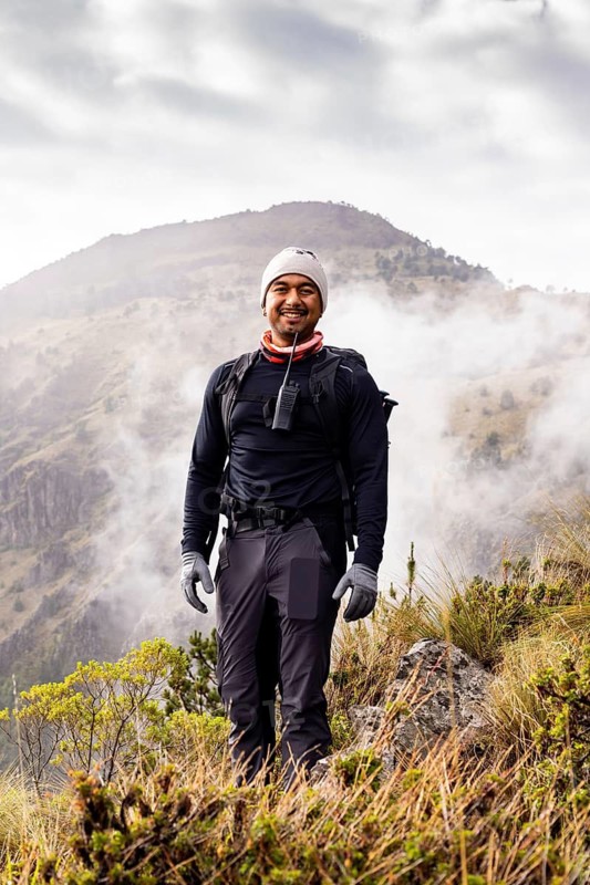 A hiker smiling in a scenic landscape with misty mountains in the background, wearing hiking gear and ready to explore the natural beauty surrounding them on a morning trek