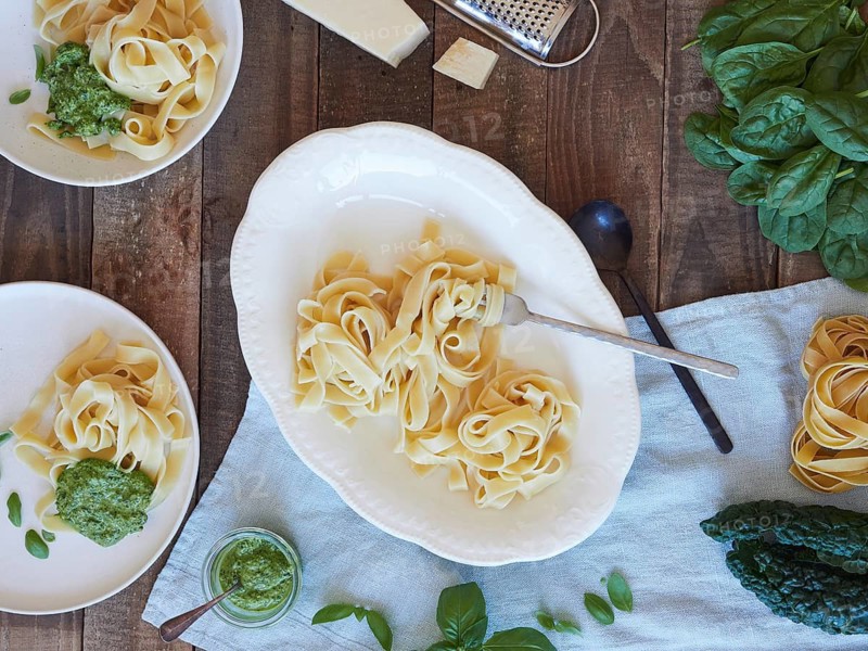 Tagliatelle pasta served at table with spinach and kale pesto beside parmesan cheese. Traditional Italian meal