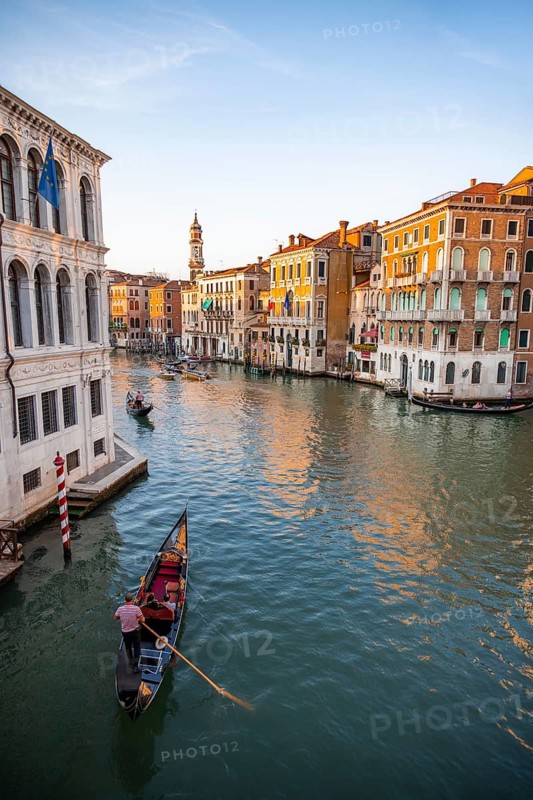 View of the Grand Canal with gondoliers at sunset, picturesque evening mood with palazzos on the canal and church tower of the Chiesa Parrocchiale dei Santi Apostoli, view from the Rialto Bridge, Venice, Veneto, Italy