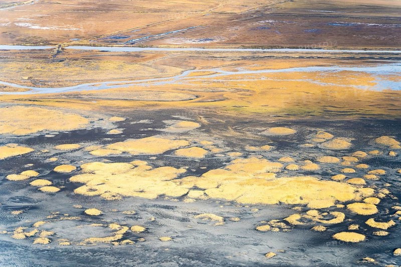 Aerial view capturing Iceland's dramatic riverbank textures, showcasing earthy tones and intricate patterns created by water flow, sediment, and natural formations