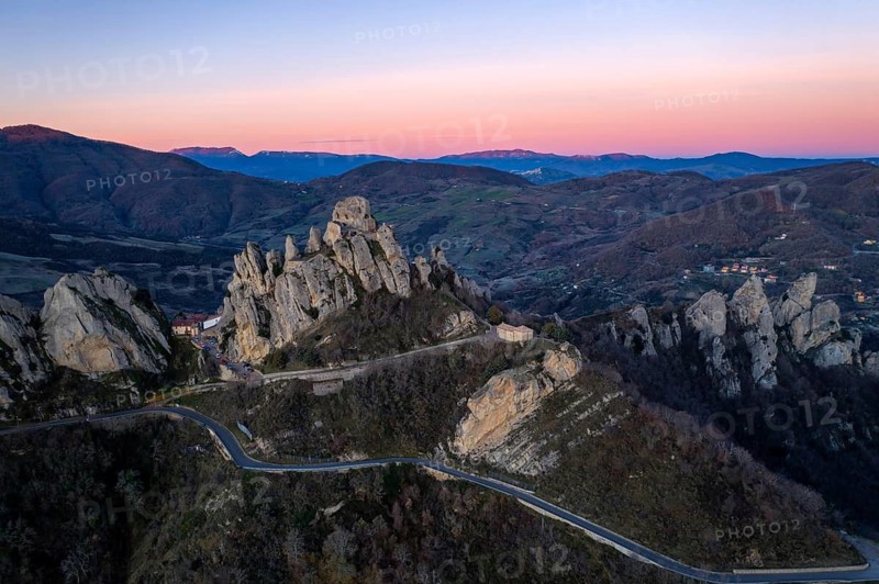 A breathtaking aerial view of Pietrapertosa, perched in the Lucanian Dolomites at sunrise. The rocky peaks and winding roads are illuminated by the soft pink and purple hues of dawn