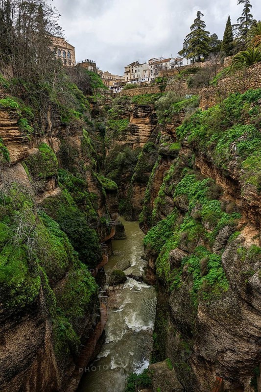 El Tajo gorge showing the Guadalevin river and a wooden walkway along the steep mossy cliffs in Ronda, Spain