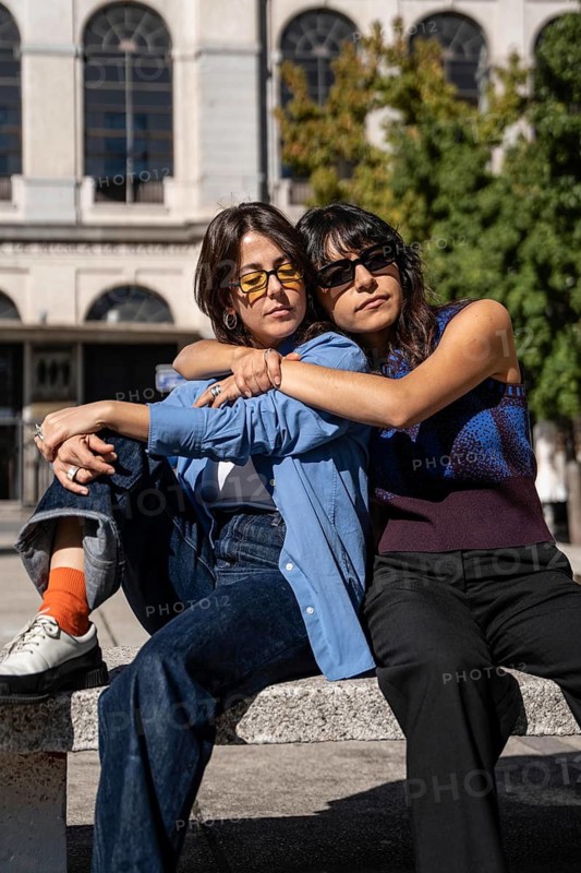 A tender scene of a multiethnic lesbian couple enjoying a shared moment outdoors. Their embrace and relaxed posture reflect love and harmony in a sunlit setting