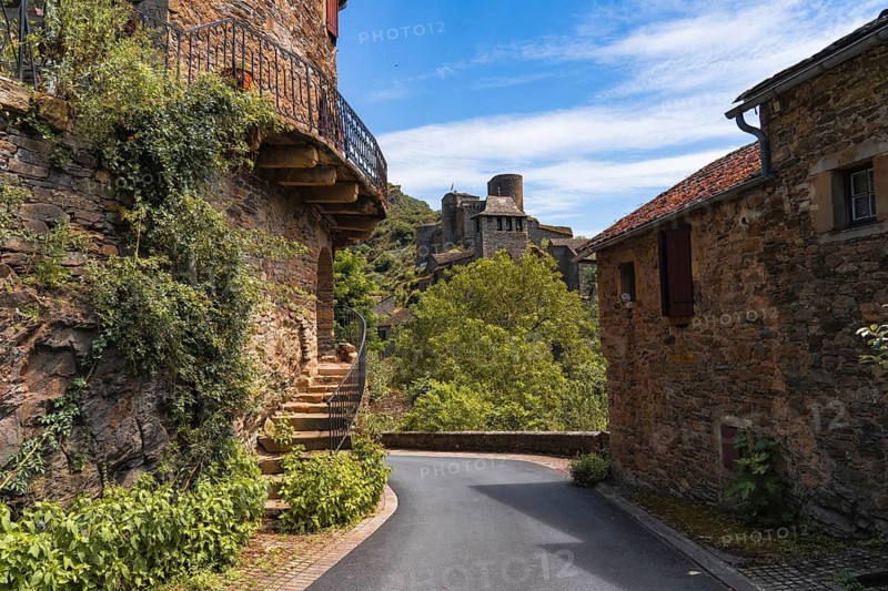 A picturesque Chateau Brousse castle medieval road in france with rustic stone houses, lush greenery, and a blue sky The scene captures the charm and tranquility of rural life in summer