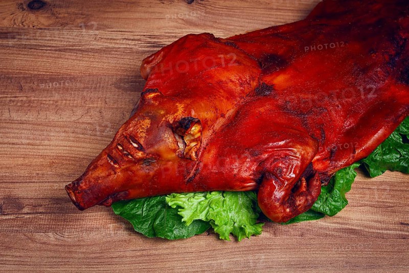 Baked, fried piglet, on a wooden table, no people, The whole piglet is baked and served on the leaves of a fresh green salad, showing off its crispy skin and detailed features