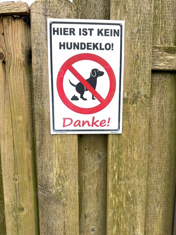 Sign with pictogram and inscription Hier ist kein Hundeklo on the outside of a wooden fence, Germany