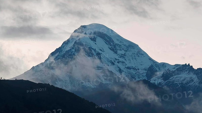 A snow-covered mountain Kazbek at dusk surrounded by clouds, Kazbegi, Stepantsminda, Georgia