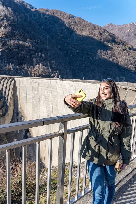 A young woman captures a selfie on a sunny winter day at the Contra Dam in Verzasca, situated in the scenic Locarno District of Ticino, Switzerland