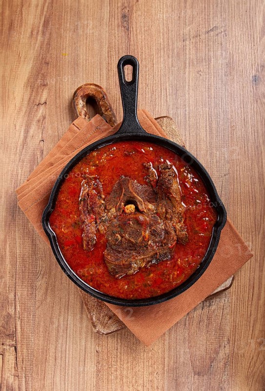Fried steak, veal neck on the bone, stewed with vegetables, in tomato sauce, cooking meat, in a cast-iron frying pan, top view, no people