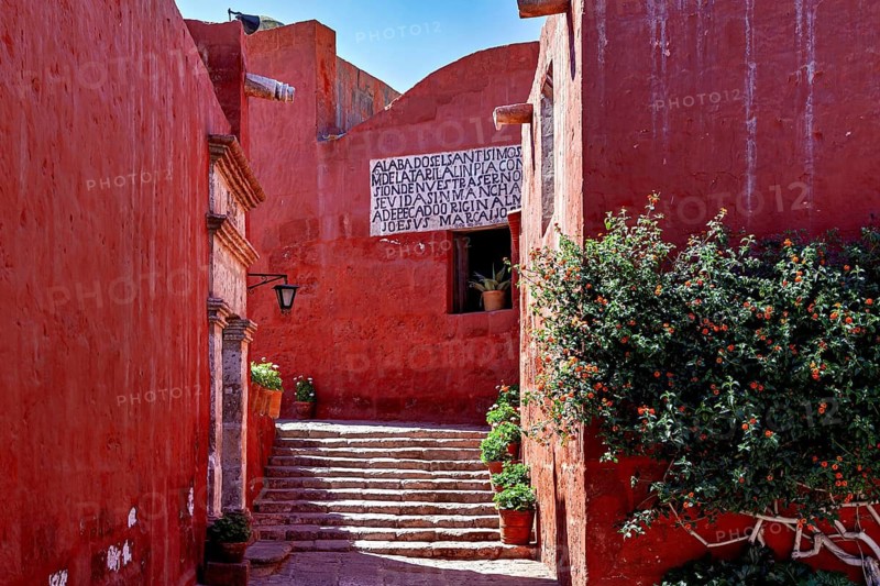 An inviting area with red walls, a staircase and green plants in the sunlight, Santa Catalina Monastery in Arequipa in Peru