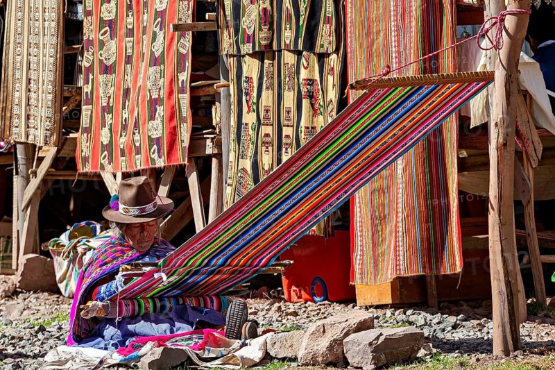 Man weaving on a colorful loom against a background of colorful fabrics, elderly traditionally dressed lady from Peru weaving a cloth