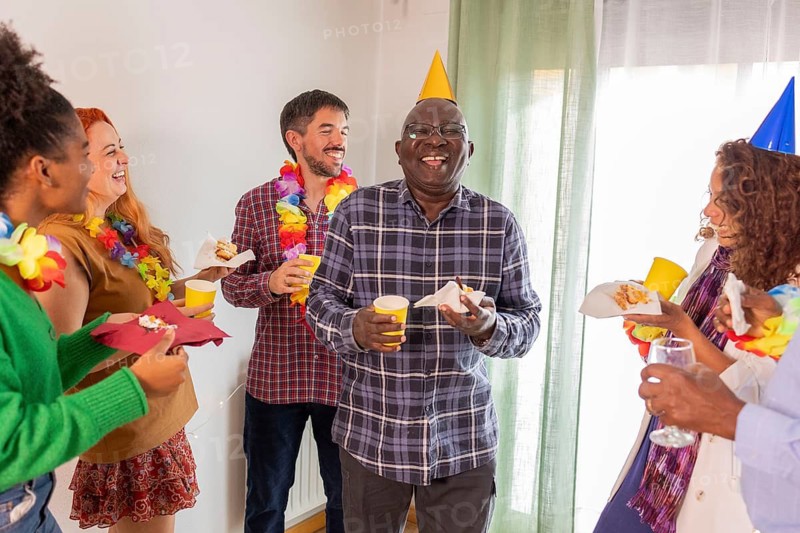 A joyful birthday party scene with friends laughing, wearing colorful leis and hats. They are enjoying drinks and cake in a lively, festive atmosphere