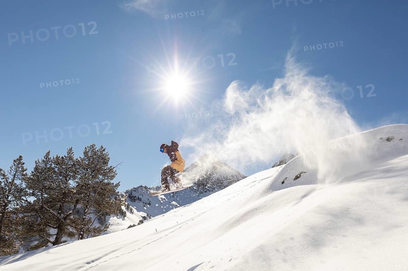A dynamic image captures a snowboarder effortlessly gliding through untouched powder in a backcountry setting. The sun shines brightly, highlighting the thrill of extreme snow sports