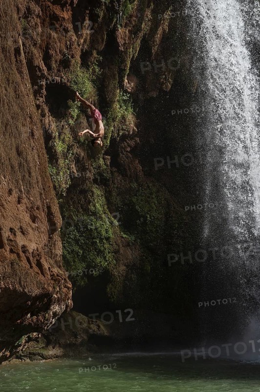OUZOUD, MOROCCO - OCTOBER 5, 2024: A Moroccan young man jumps from the high rock into the water under a waterfall Ouzoud