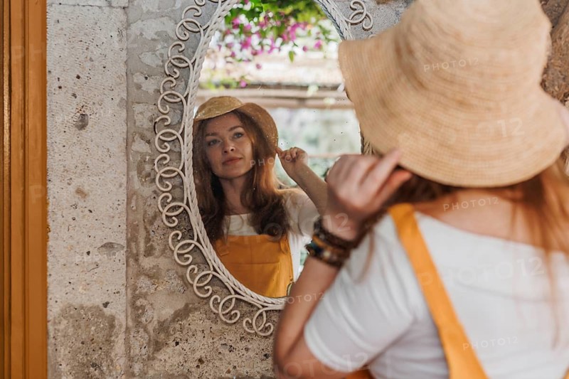 A woman traveler in a yellow overall and hat enjoys her vacation, admiring her reflection in a vintage mirror in a picturesque old town in Turkey. The scene captures the charm and beauty of travel