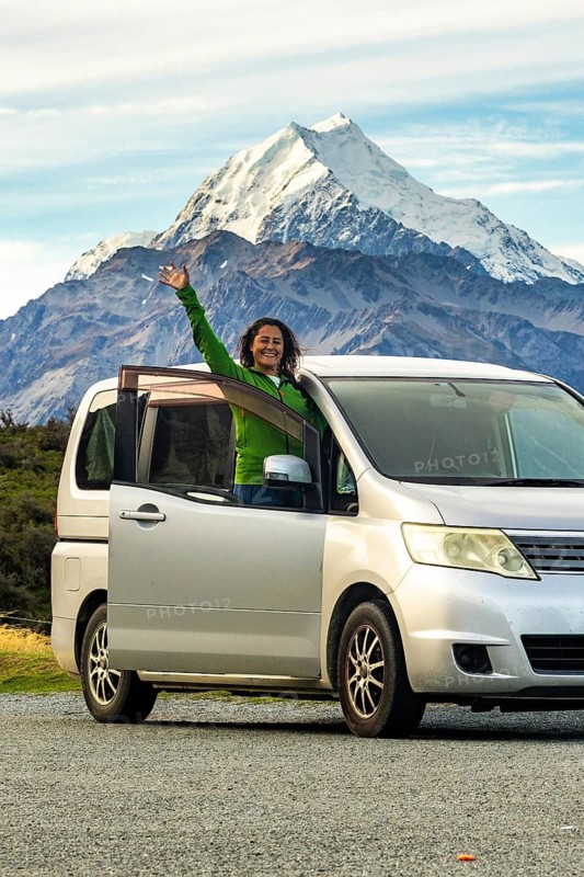 A woman stands joyfully by her car in autumn at Mount Cook, New Zealand. The majestic mountain provides a stunning backdrop to the joy of travel and nature exploration