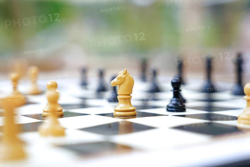 A close-up of a chessboard outside, featuring white and black chess pieces in focus The blurred background emphasizes the strategic atmosphere of the game
