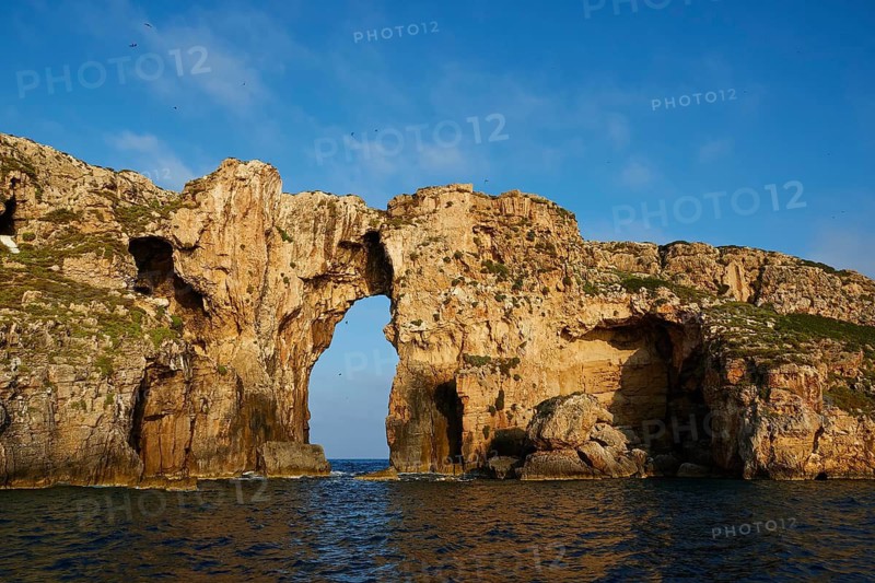 A majestic rock arch dominates the landscape, surrounded by blue sea under a clear sky, morning light, Tsichli Babas islet, Navarino Bay, Pylos, Peloponnese, Greece