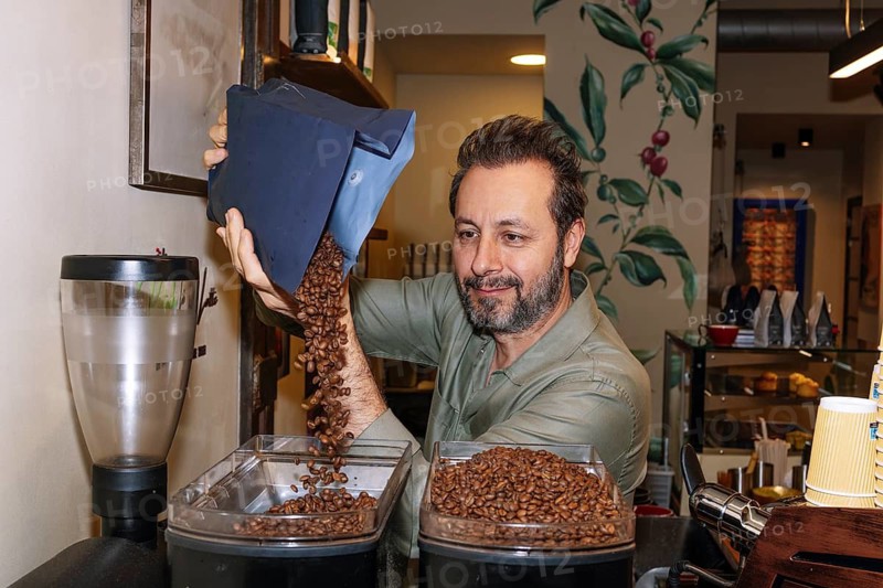 A coffee artisan pours specialty beans into a grinder in a cozy cafe. The setting highlights attention to detail in crafting high-quality coffee experiences for enthusiasts and connoisseurs
