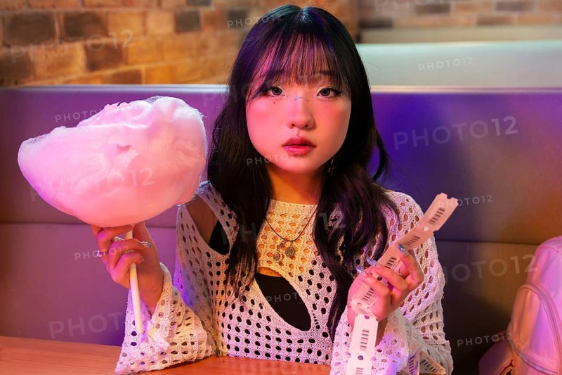 Asian Gen Z girl enjoys a fun day, holding cotton candy and tickets The vibrant setting reflects her excitement and youthful spirit