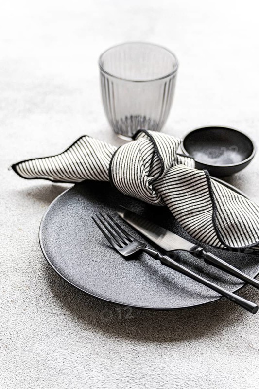 Black and white table setting featuring a textured plate, striped napkin, sleek cutlery, and a transparent glass. Perfect for minimalist or modern dining themes