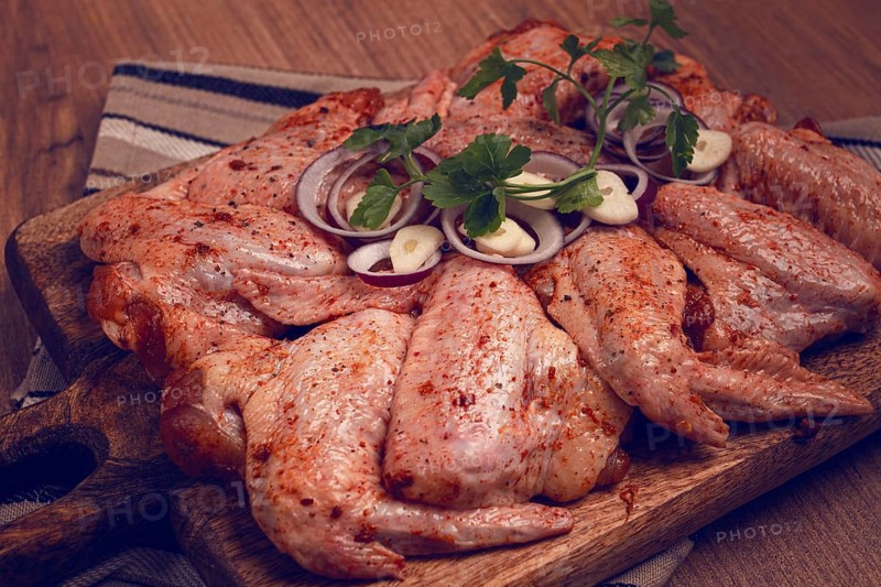 Chicken wings, marinated and laid out on a wooden platter, ready for cooking, grilling or baking, in a home kitchen, there are no people