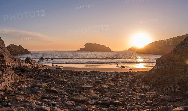 Golden light from the rising sun reflects across the wet sand and coastal rocks of Arnia Beach, Costa Quebrada, creating a magical and tranquil seaside scene in Cantabria