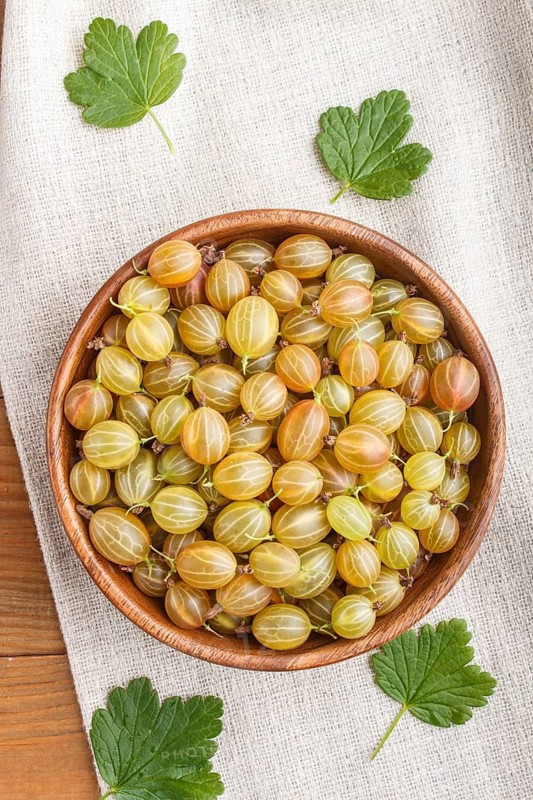 Fresh green gooseberry in wooden bowl on wooden background. top view, flat lay, close up