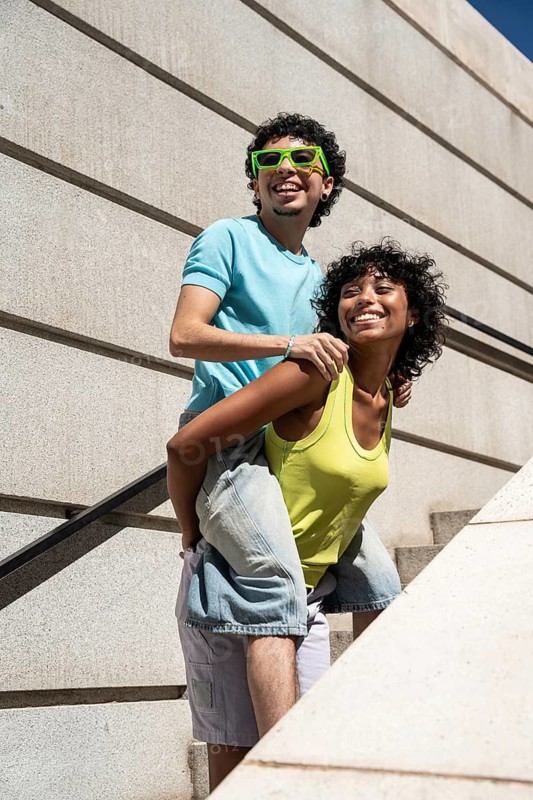 A lively multiethnic LGBTQ+ couple shares a joyous moment outdoors, showcasing happiness and diversity. The essence of love and freedom is captured in their cheerful expressions