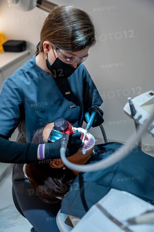 Dentist using specialized equipment for teeth whitening procedure on patient, demonstrating professional dental care in a modern clinic setting
