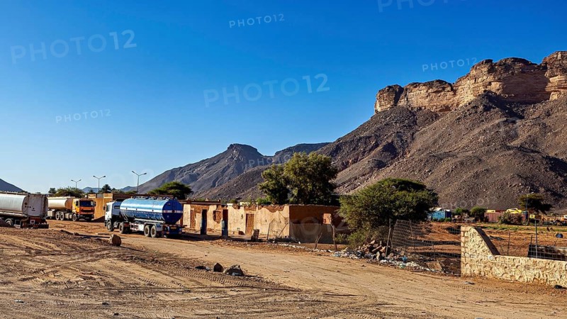 Lorry on a road in front of a mountain landscape in dry surroundings, settlement in the Sahara in Algeria