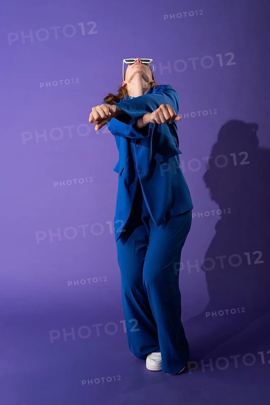 A young woman in a vibrant blue outfit dances gracefully against a vivid purple background. Her confident pose and dynamic movement capture the essence of modern dance