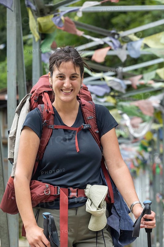 Smiling woman with a backpack and trekking gear stands on a path adorned with prayer flags, ready to embark on an adventure along the trails of Mount Everest