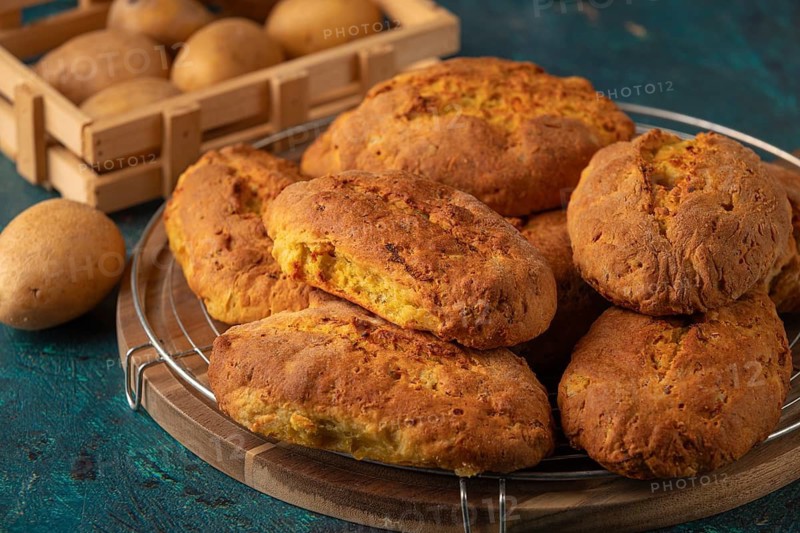Freshly baked potato rolls with golden brown crust on a wooden board, potatoes in the background
