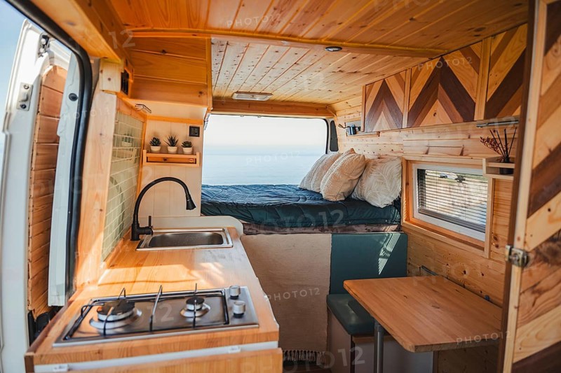 Cozy camper interior perfect for traveling and teleworking. Featuring a wooden finish, a small kitchenette, and a comfy sleeping area overlooking a scenic view, it offers comfort and function