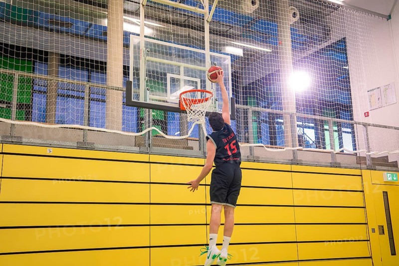 A player performs a dunk in a yellow gym in good light, basketball TSV Calw, Germany