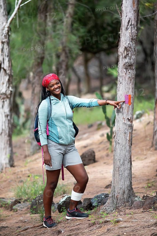 Mauritian woman, 35 years old, showing a hiking trail marker in a casuarina forest, Rodrigues Island, Mauritius