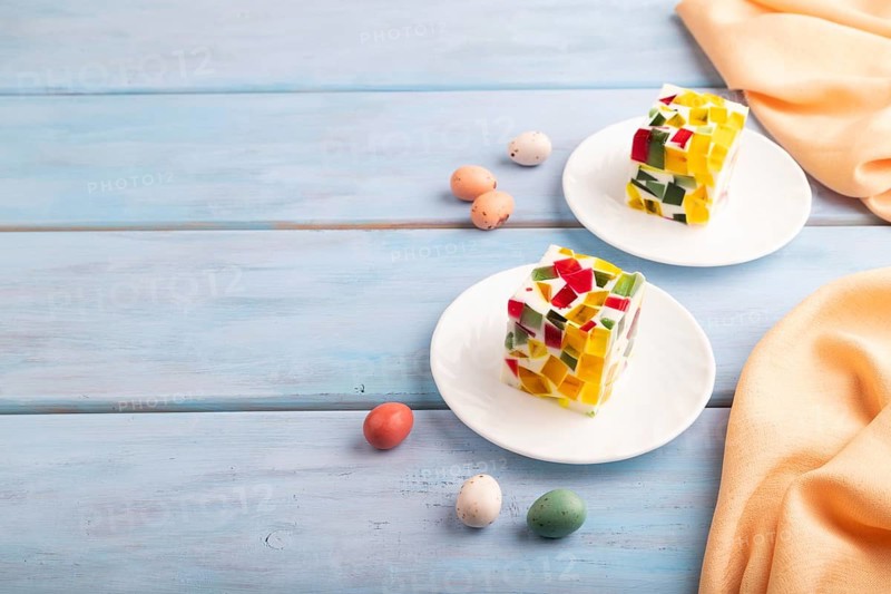 Colored Fruit and milk jelly on blue wooden background and orange linen textile, side view, copy space