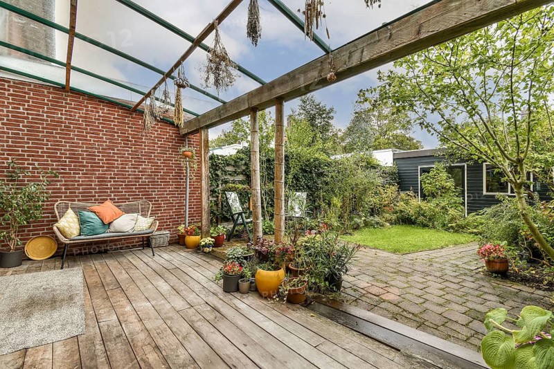 A charming backyard patio features wooden decking, cozy seating, and colorful potted plants. Surrounded by lush greenery, it offers a peaceful outdoor retreat for relaxation