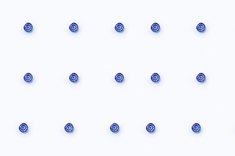 A minimalist image showing thirteen small blue Murano glass marbles arranged in a grid on a crisp white background. These delicate pieces are handcrafted in Venice, Italy