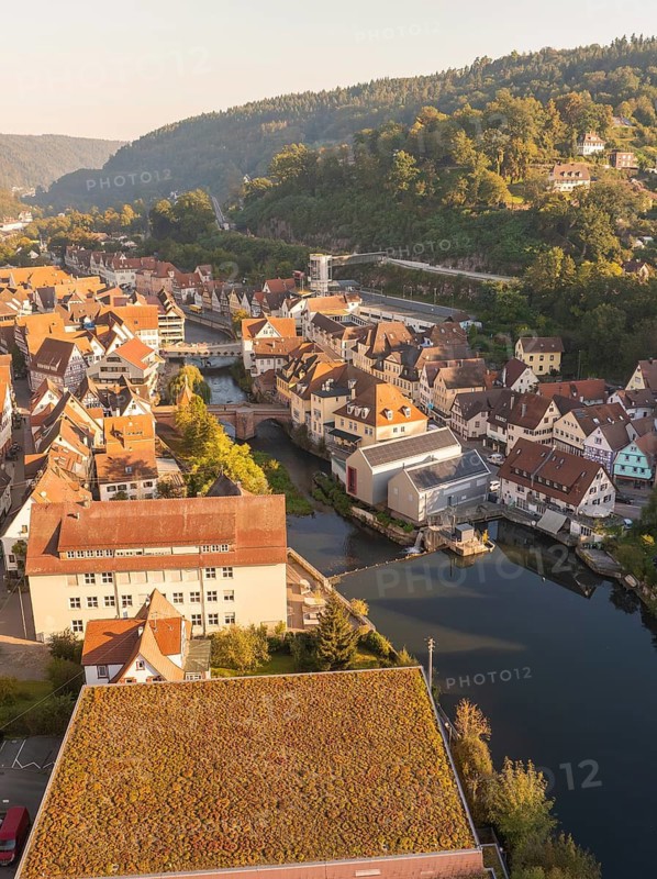 Bird's eye view of a town with traditional buildings along a river, overgrown roofs and road in the foreground, green hills in the background, Calw, Black Forest, Germany