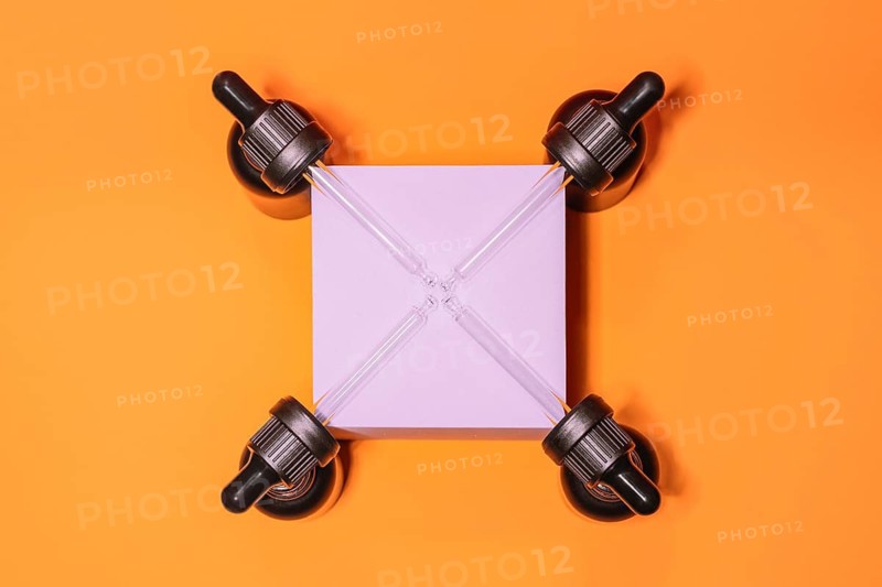 Four droppers symmetrically positioned around a pink square on a vibrant orange background, creating a striking geometric pattern. Ideal for modern design concepts