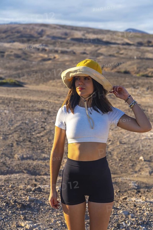 Young woman adjusting her hat while enjoying the scenic view of a volcanic landscape in gran canaria, spain