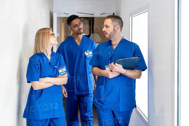 Diverse medical team collaborating and communicating while walking through a bright hospital corridor, showing healthcare professionals working together in a modern clinic environment