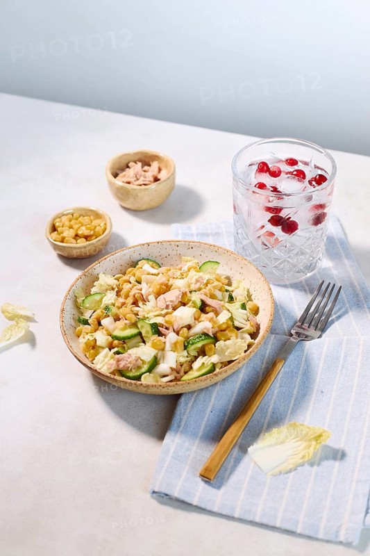 A vibrant tuna salad featuring cucumber, corn, and cabbage in a rustic bowl. Served with a refreshing drink garnished with red berries, this meal offers a perfect balance of color and flavor